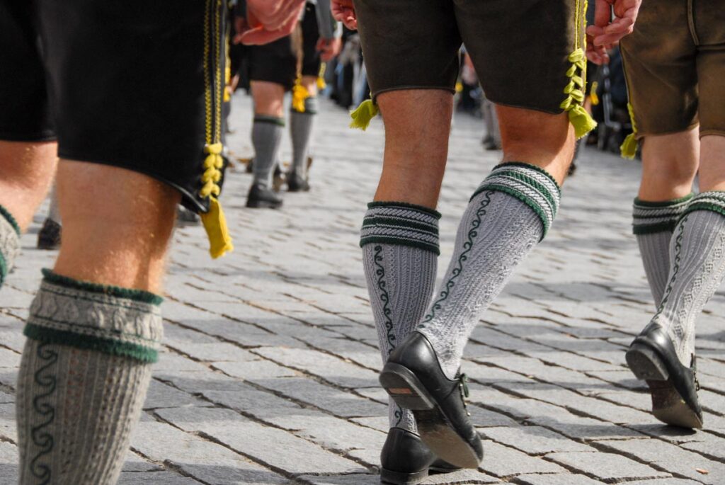 Close-up of men walking in an Oktoberfest parade in Munich, wearing traditional Bavarian knee-high socks with green embroidery, black shoes, and lederhosen adorned with yellow tassels.
