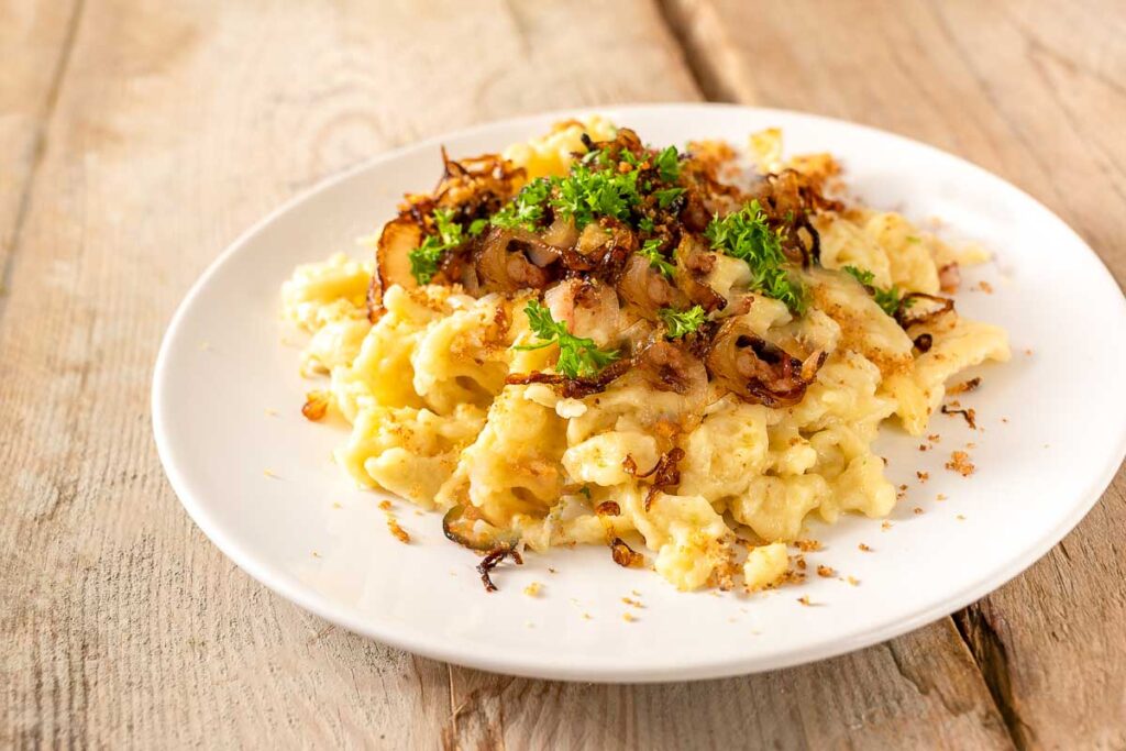 Creamy German cheese noodles known as Käsespätzle, topped with crispy onions and fresh parsley—comforting vegetarian option at Oktoberfest food.
