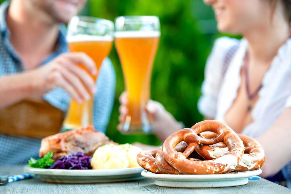 A table with pretzels, hearty Bavarian food, and wheat beer in tall glasses.