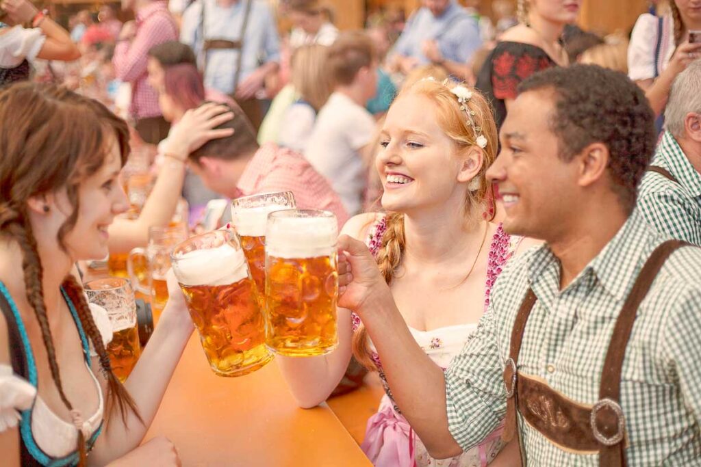 Friends in dirndl and lederhosen clinking large beer mugs in a festive beer hall at the Oktoberfest in Munich