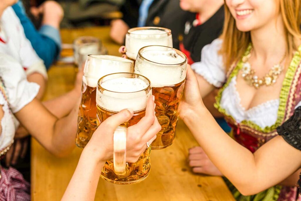 Close-up of hands holding and toasting with beer mugs at a wooden Oktoberfest table.