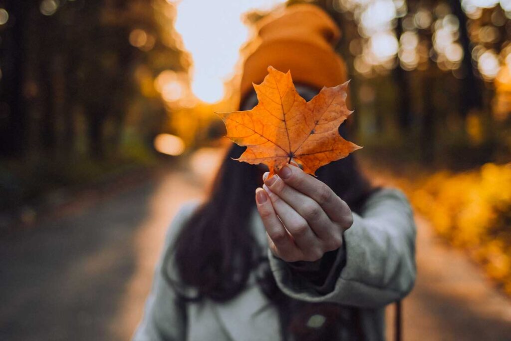 A woman holding a fall leave in orange in front of her face