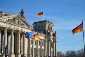 Berlin’s historic Reichstag building, topped with German flags and adorned with neoclassical columns, displays the phrase “Dem Deutschen Volke” above its entrance.